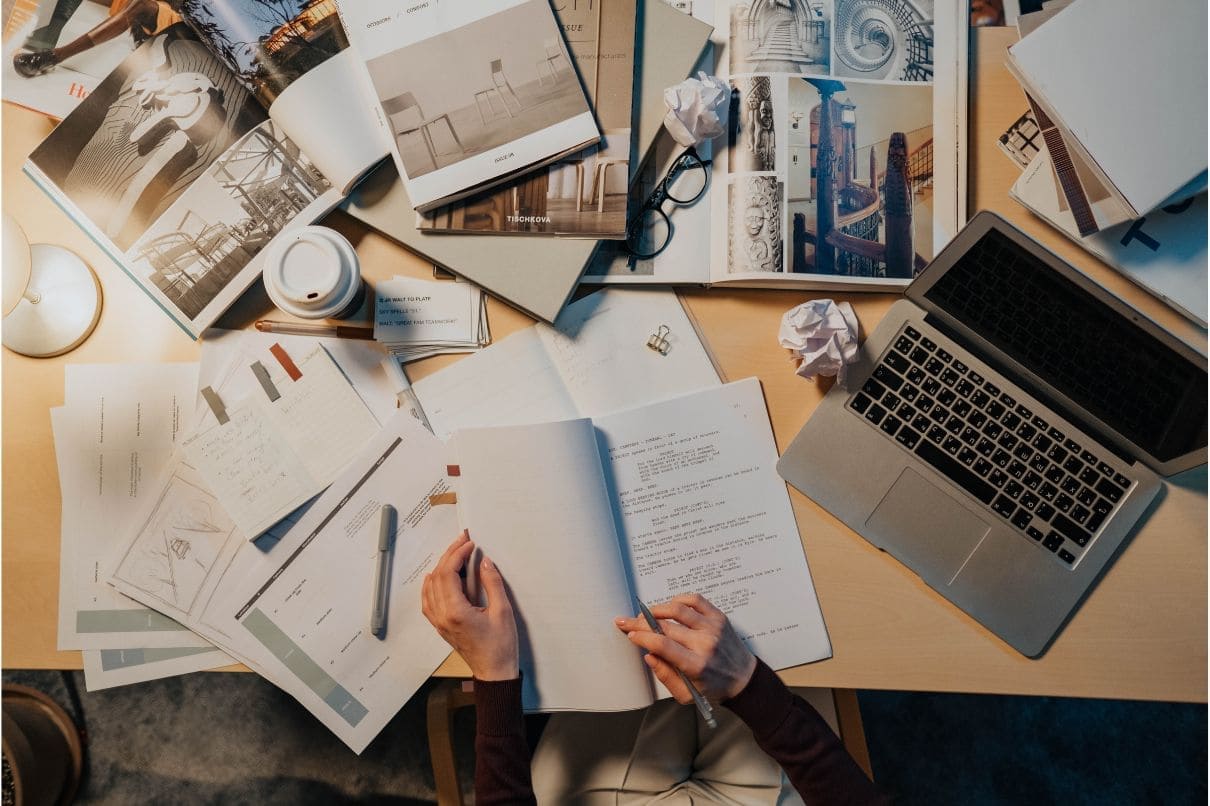 A person working at a desk with papers, laptop, and laptop.